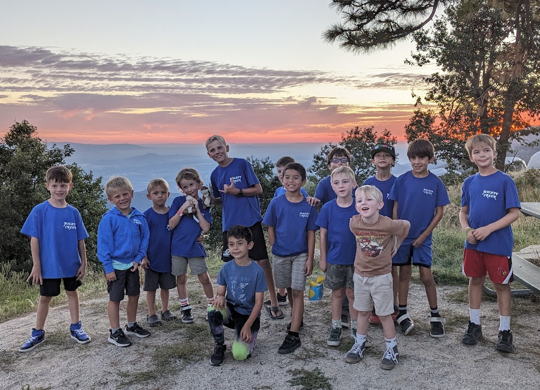 Mighty Creek boys in blue shirts posing at a mountain overlook at sunset